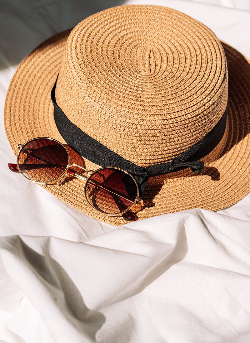 Sombrero de paja con unas gafas de sol encima de una sábana blanca.